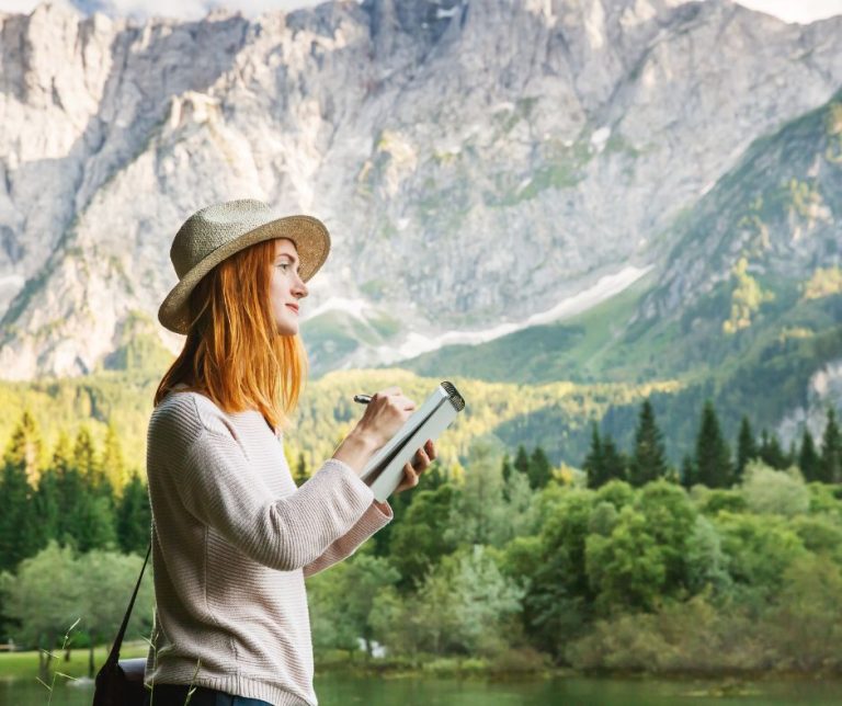 Woman nature journaling with large mountains and forest around her