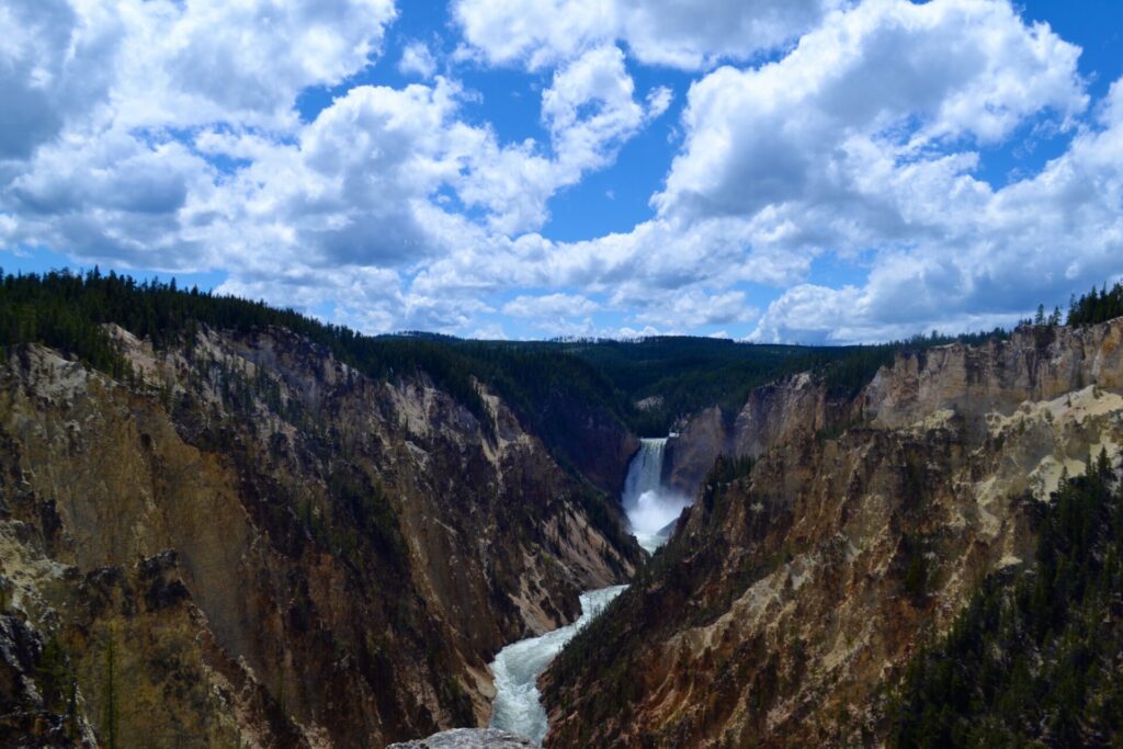 Yellowstone River and waterfall running through the Grand Canyon of the Yellowstone with blue sky and white clouds above.