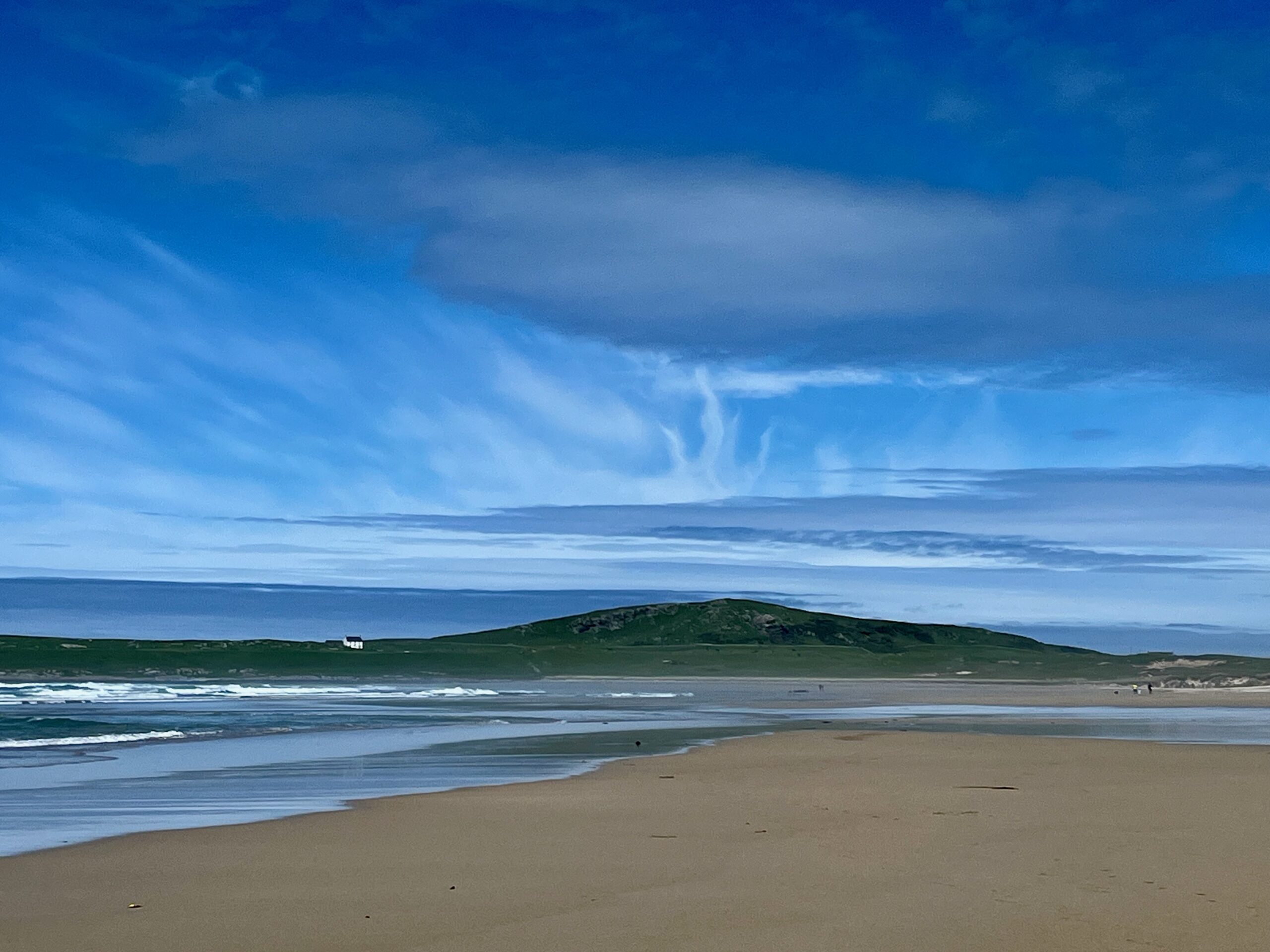 Machir Bay, Islay, Scotland. Sandy beach, waves, hillside with white cottage evoking books in Scotland. Dramatic clouds above